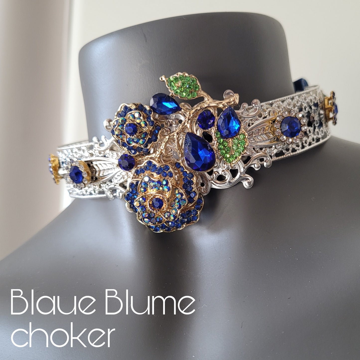 A choker necklace in silver metal adorned with crystal encrusted blue rose with leaves, and sparkling glass crystals in matching shades.