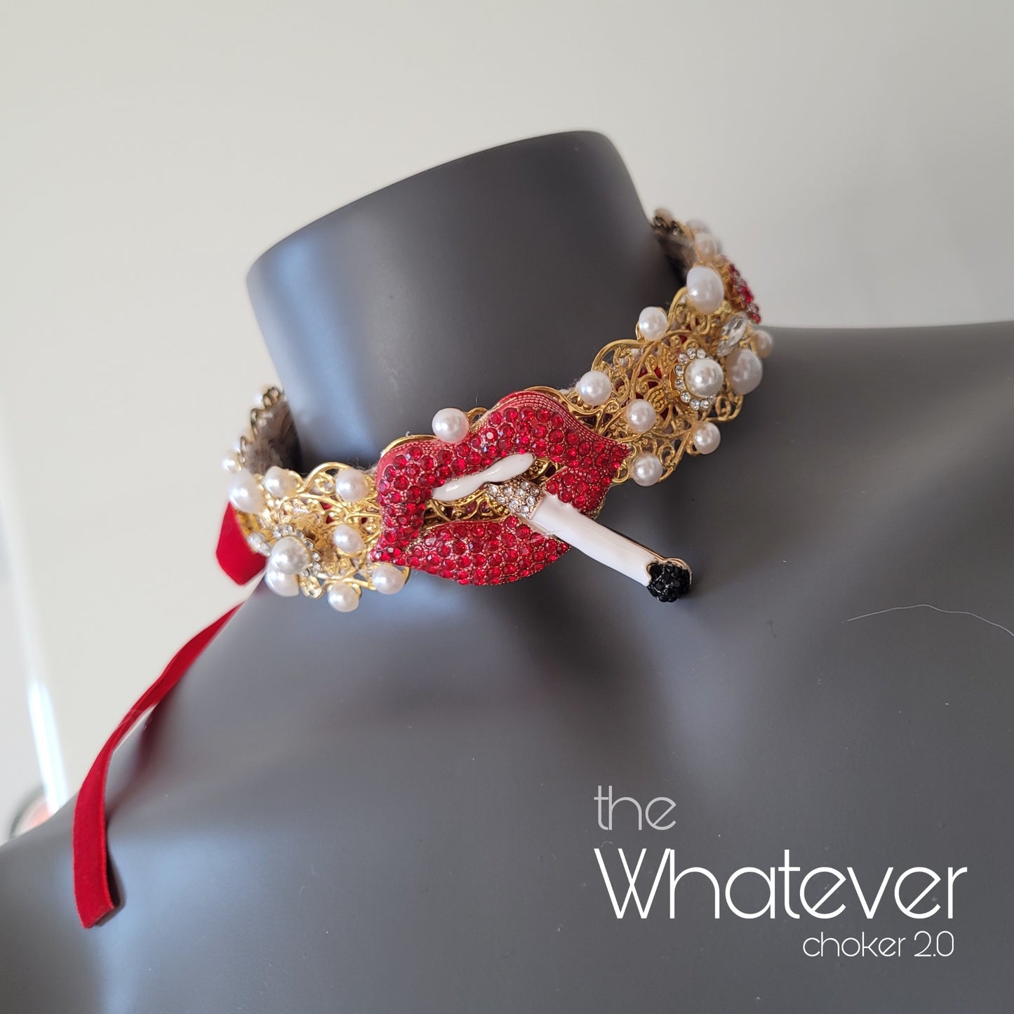 A choker necklace in golden metal adorned with red crystal encrusted lips, a cigarette, sparkling glass crystals and faux pearls.