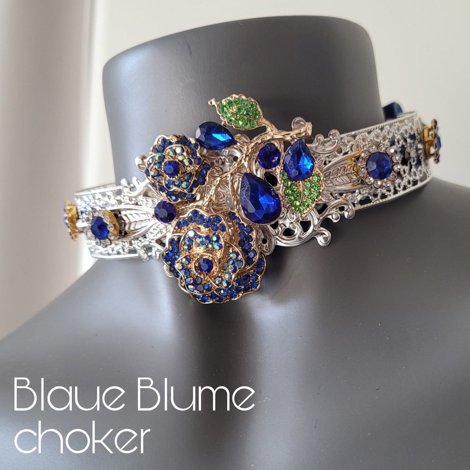 A choker necklace in silver metal adorned with crystal encrusted blue rose with leaves, and sparkling glass crystals in matching shades. 