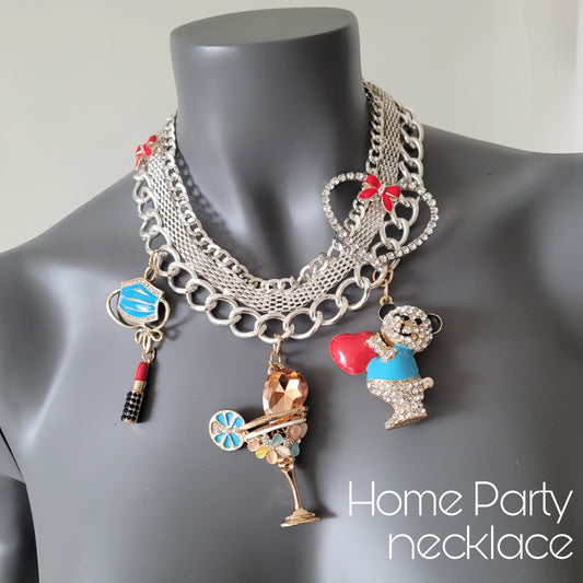 WhatEver collection: The Home Party metal necklace in silver coloured metal adorned with a crystal heart, red ribbons, and various crystal encrusted pendants including a face mask, lipstick, bear holding a heart, and a drink