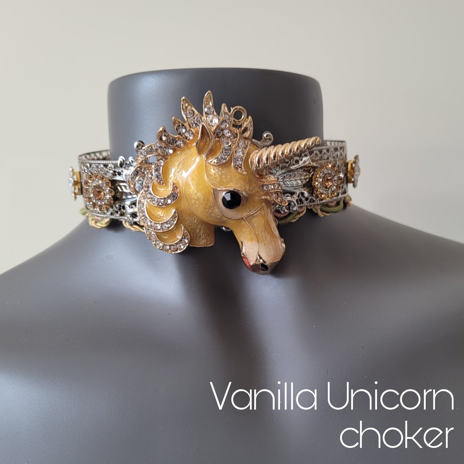 A choker necklace in silver metal adorned with a cream unicorn head and sparkling glass crystals, and decorative trim in matching shades. 