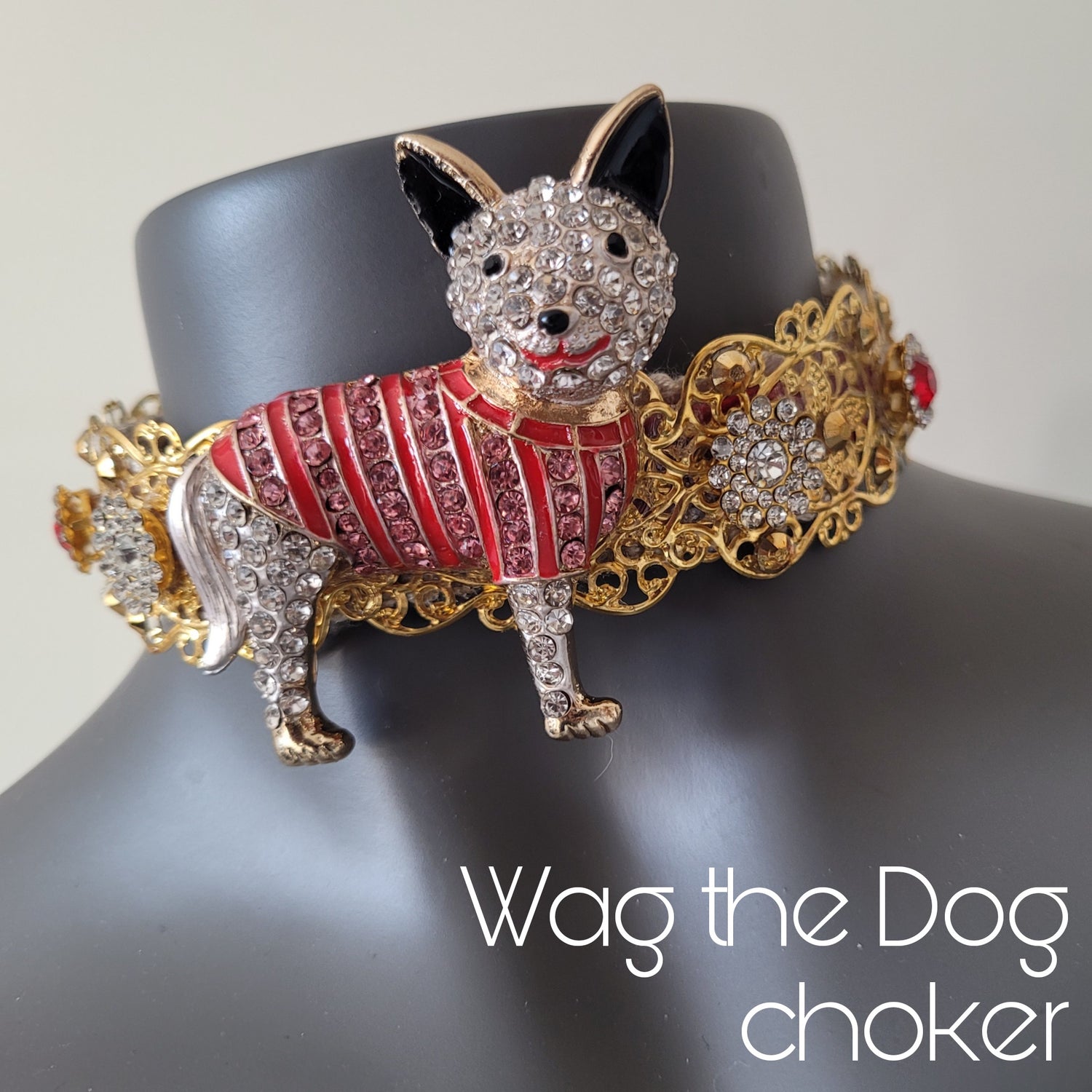 A choker necklace in golden metal adorned with crystal encrusted boxer dog wearing a red and pink jacket, and sparkling glass crystals. 